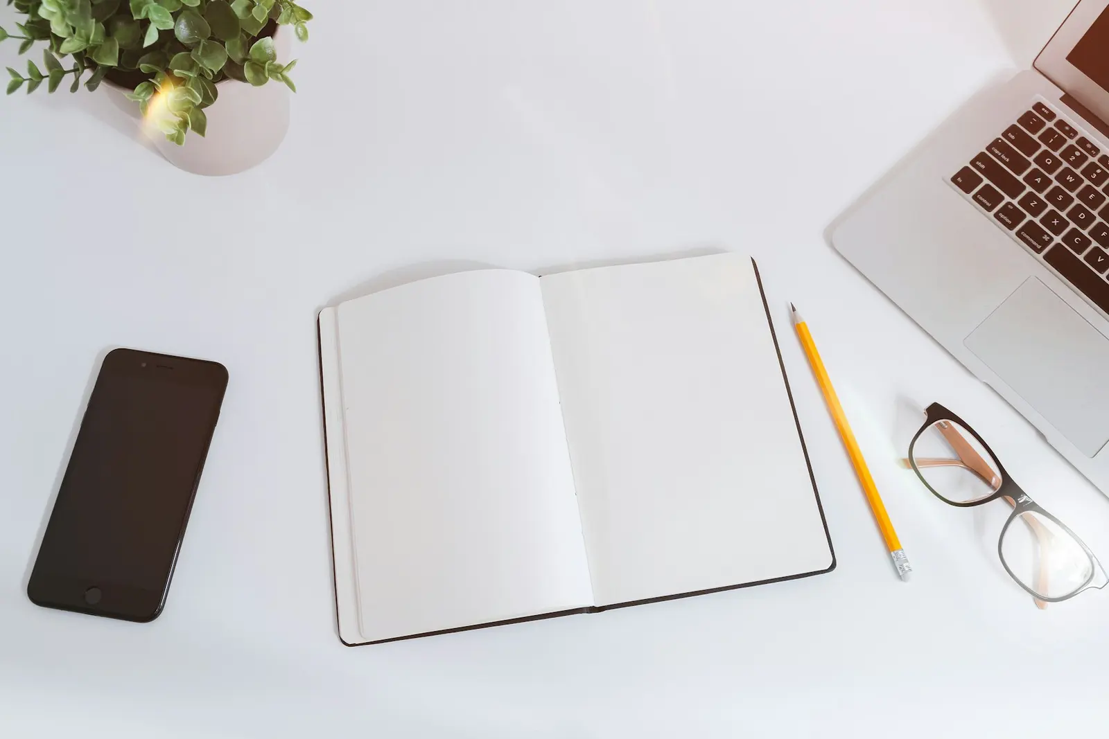 Open notebook, laptop and phone on a white desk