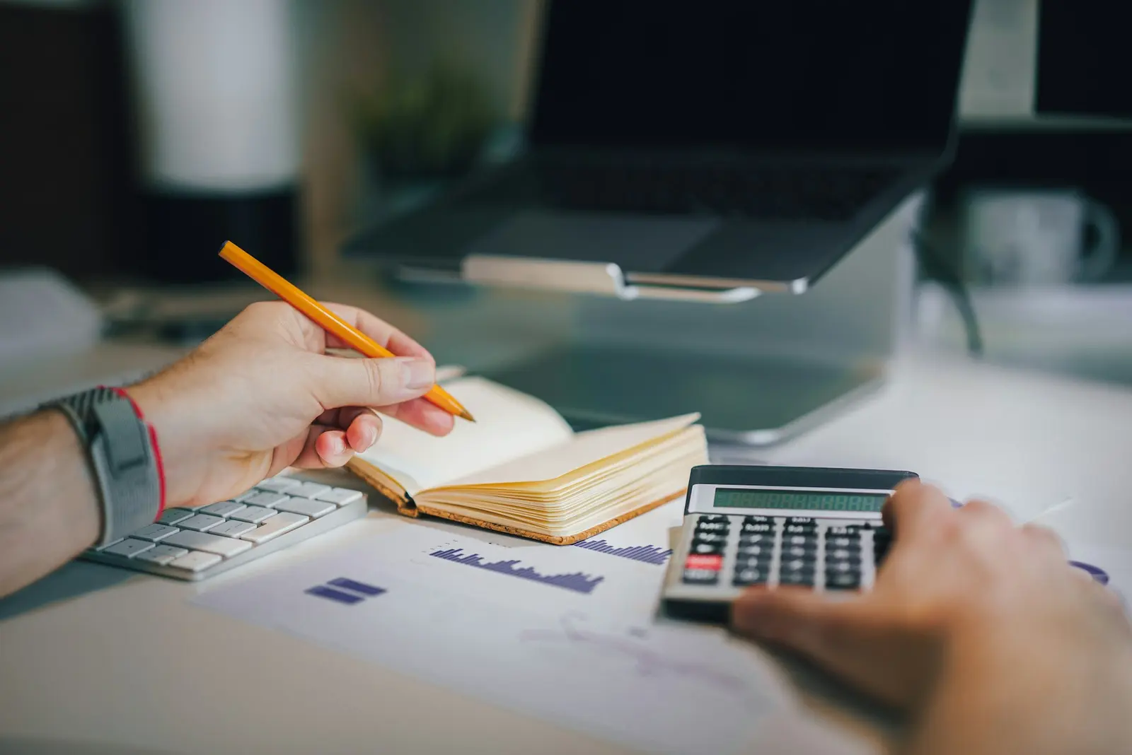Hands using a calculator beside a notebook